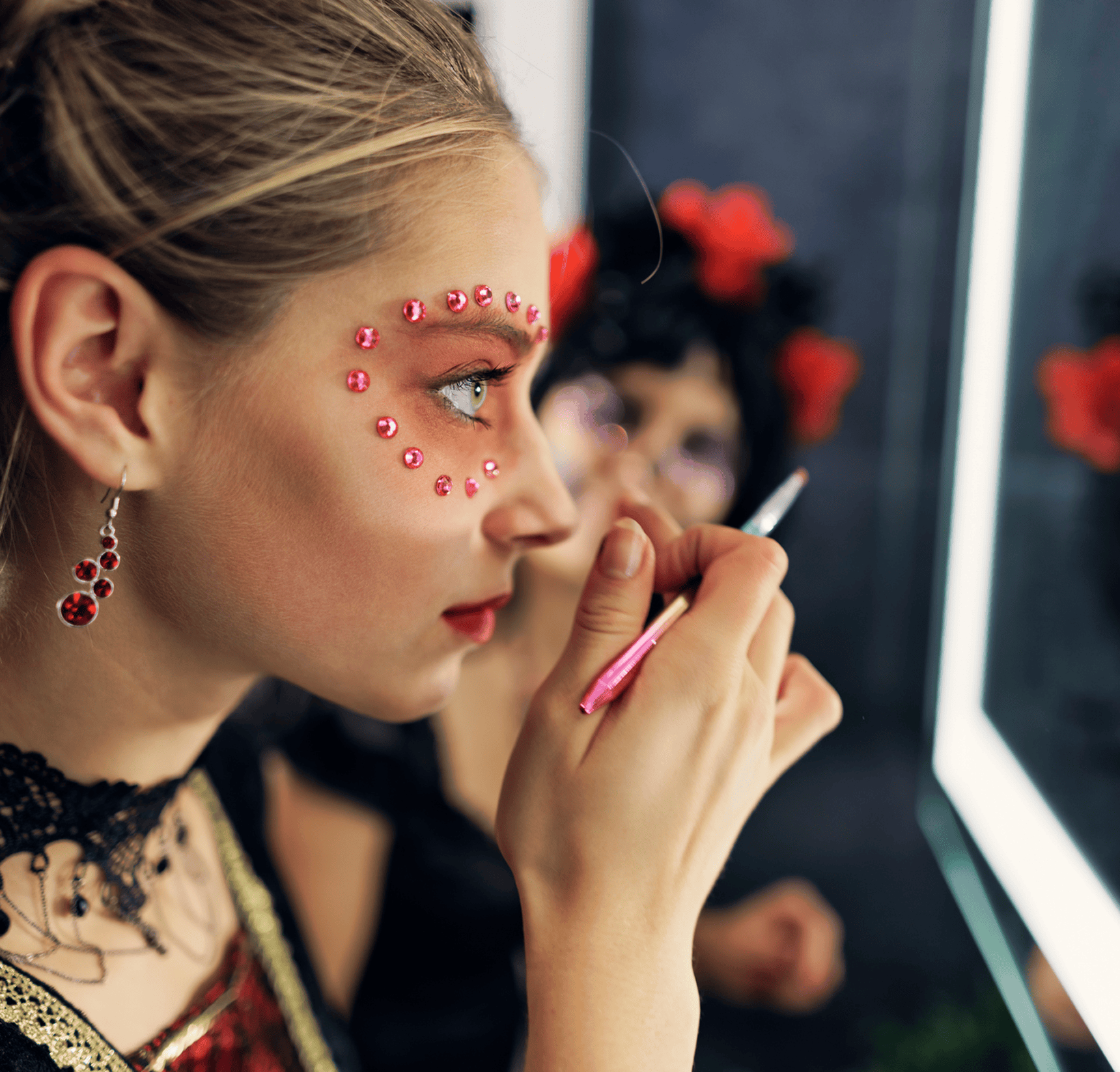 Woman applying makeup with jeweled face design.