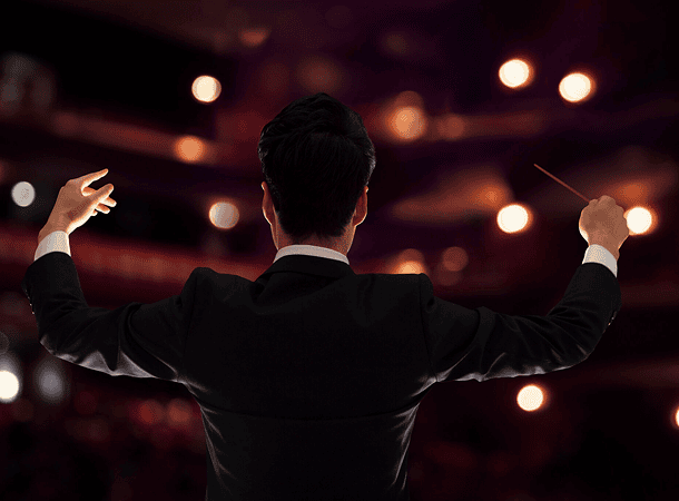 Conductor leading orchestra in dimly lit venue.